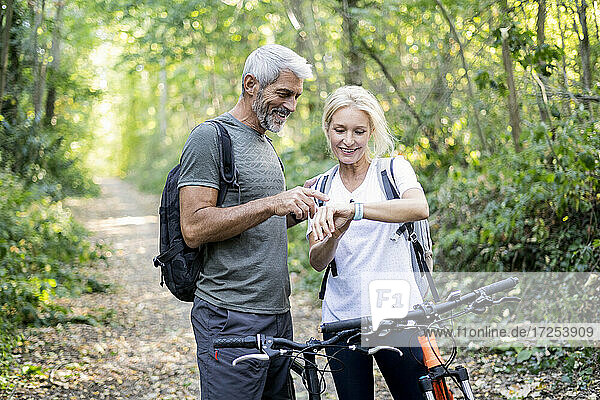 Smiling mature couple checking direction on smart watch in forest