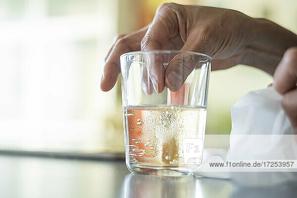 Close-up of woman's hand dropping pill in glass of water