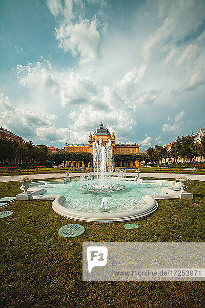 Blick auf eine Wasserfontäne mit dem Kunstpavillon in Zagreb im Hintergrund