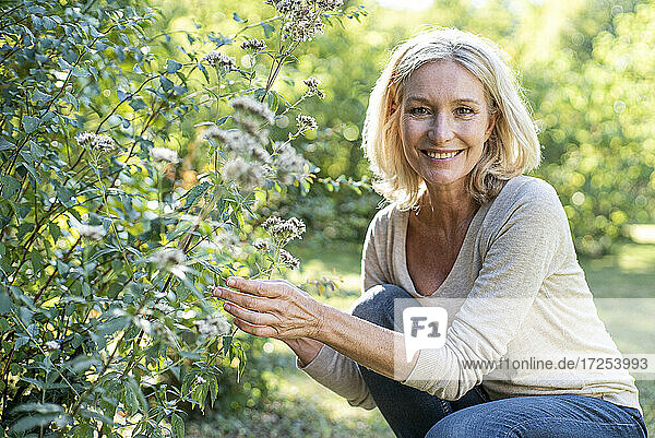 Porträt einer lächelnden reifen Frau  die eine Pflanze im Hinterhof berührt