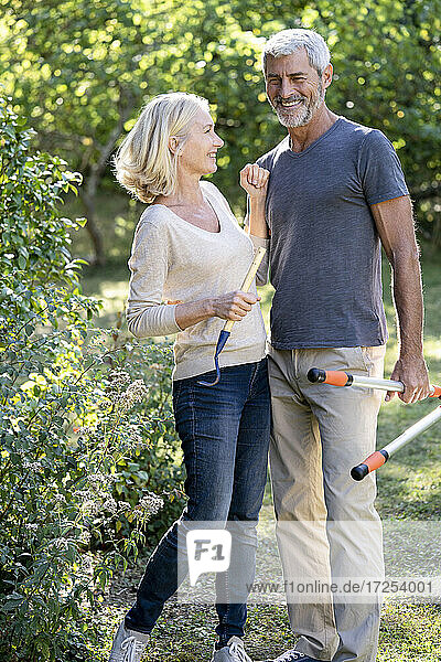 Smiling mature couple with gardening equipment standing in backyard