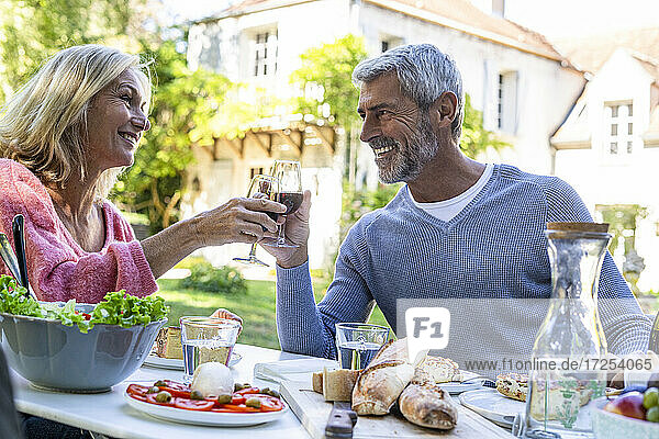 Lächelndes reifes Paar  das am Tisch sitzend mit Weingläsern anstößt