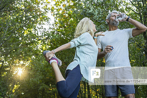 Low angle view of smiling mature couple exercising and drinking water in forest