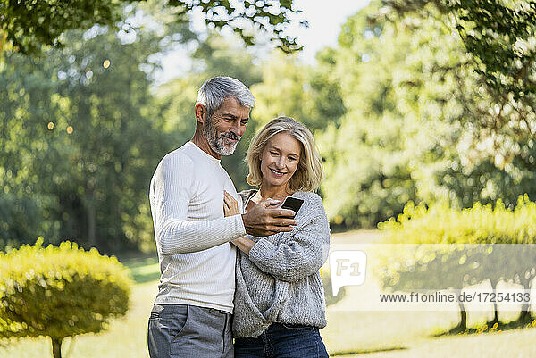Smiling mature couple using smartphone in backyard