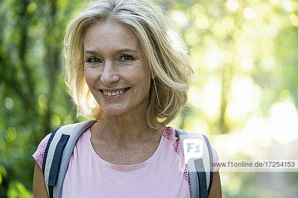 Portrait of smiling mature woman with backpack in forest