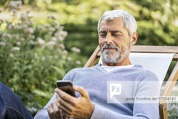 Smiling mature man using smartphone while sitting on deckchair