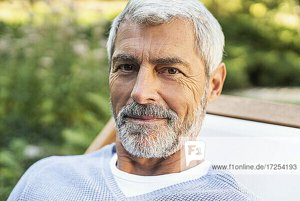 Porträt eines lächelnden reifen Mannes  der im Hinterhof sitzt