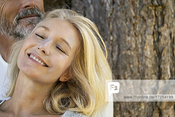 Nahaufnahme eines lächelnden reifen Paares  das sich an einen Baumstamm lehnt