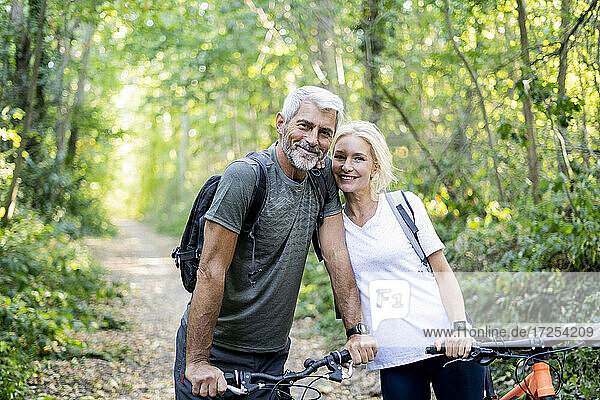 Porträt eines lächelnden reifen Paares mit Fahrrädern  das im Wald steht