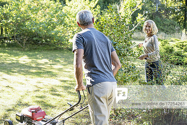 Glückliches reifes Paar mäht den Rasen und schneidet Pflanzen im Hinterhof