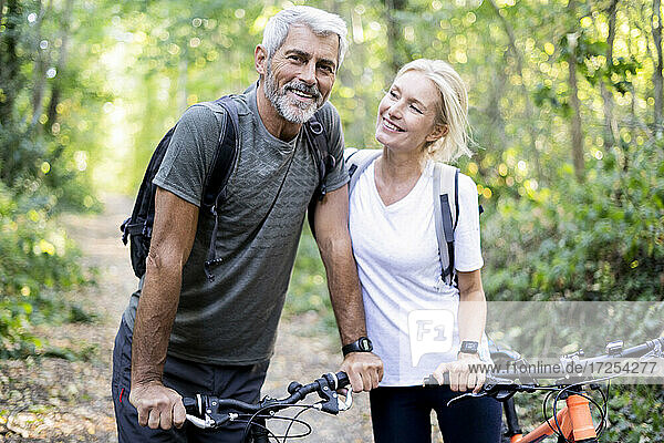 Smiling mature couple with bicycles standing in forest