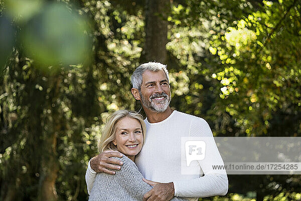 Lächelndes reifes Paar schaut weg  während es sich im Hinterhof umarmt