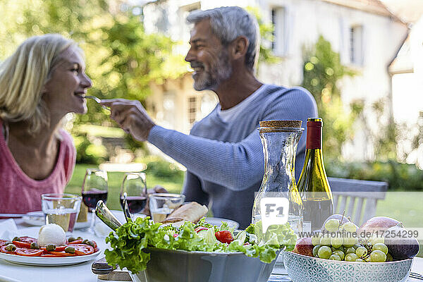 Smiling mature man feeding his wife with food on table in foreground