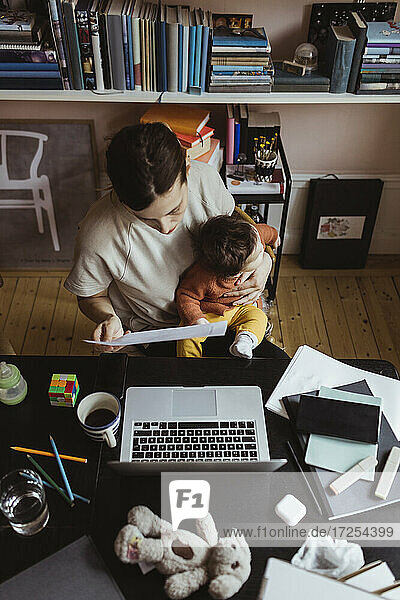 Weibliche Unternehmerin  die ein Dokument liest  während sie mit einem kleinen Jungen im Büro zu Hause sitzt