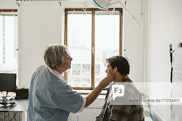 Älteres weibliches Pflegepersonal untersucht den Hals eines männlichen Patienten in einer medizinischen Klinik