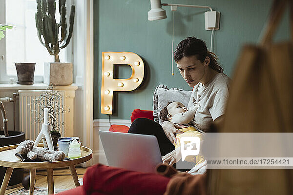 Weiblicher Profi  der am Laptop arbeitet  während er sich um einen kleinen Jungen zu Hause kümmert
