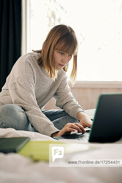 Teenage girl typing on laptop while doing homework at home