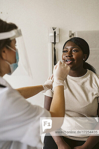 Weibliche Gesundheitshelferin bei der Entnahme einer Probe aus dem Mund eines Patienten in einer medizinischen Klinik während COVID-19