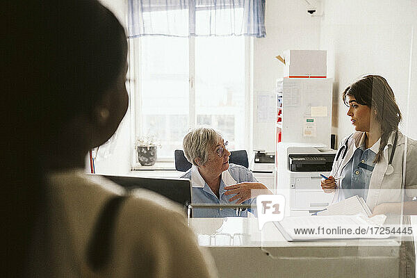 Senior female nurse discussing with doctor seen through glass at medical clinic