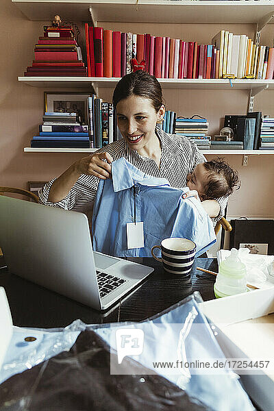 Lächelnde weibliche Unternehmerin zeigt Hemd auf Videoanruf durch Laptop bei der Arbeit im Home-Office