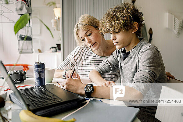 Mother guiding son doing homework while sitting at table