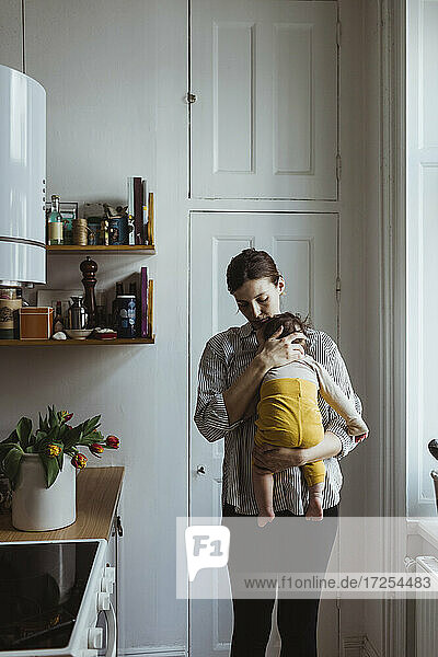 Mother carrying baby boy while standing in kitchen