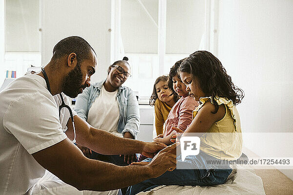 Mutter und Töchter schauen auf den männlichen Arzt  der die Hand des Mädchens in der medizinischen Klinik untersucht