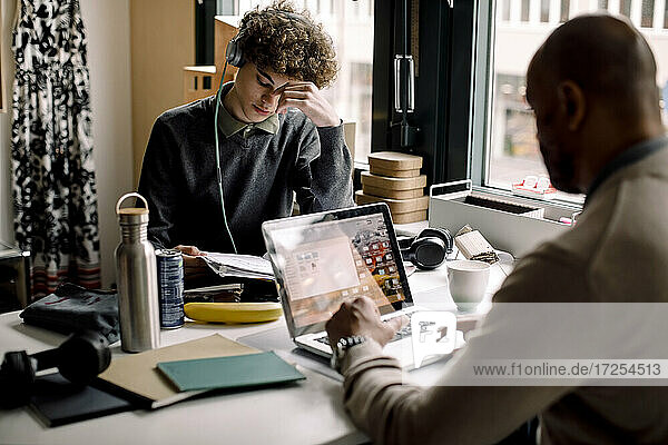 Junge trägt Kopfhörer studieren  während mit Geschäftsmann mit Laptop am Schreibtisch sitzen