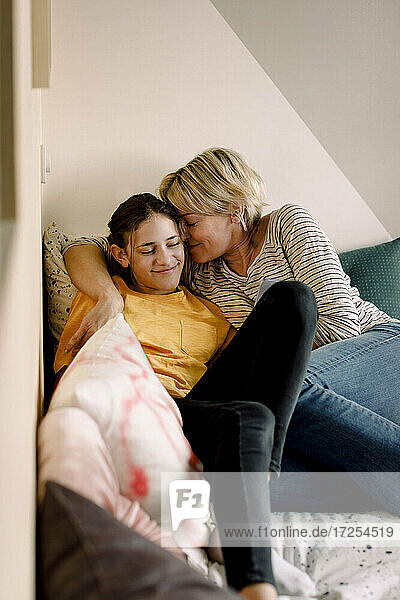 Smiling mother and daughter lying on bed at home