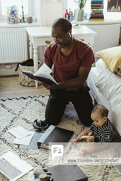 Männlicher Unternehmer kniend beim Lesen Tagebuch von Sohn zu Hause