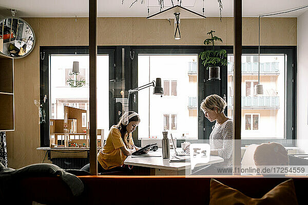 Female professional and daughter sitting at desk seen through glass