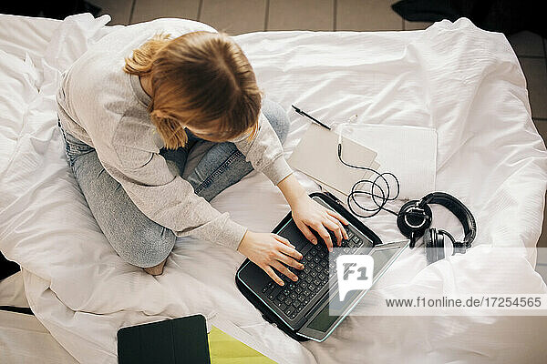 Mädchen macht Hausaufgaben  während mit Laptop im Schlafzimmer zu Hause