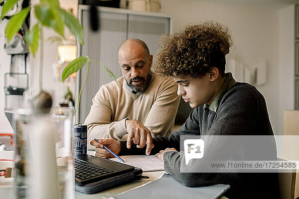 Vater leitet Sohn bei den Hausaufgaben an  während er am Tisch sitzt