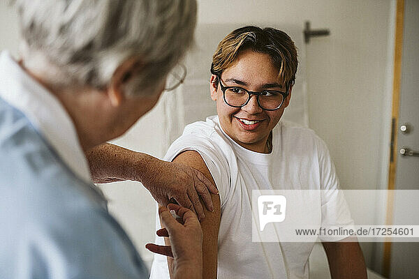 Lächelnd männlichen Patienten Blick auf ältere weibliche Arzt geben Impfstoff in der medizinischen Klinik