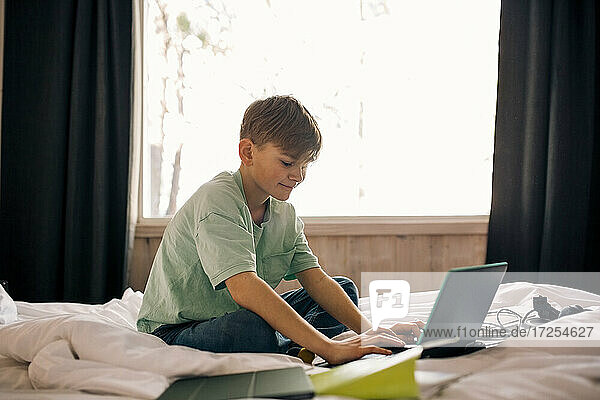 Boy using laptop while doing homework in bedroom