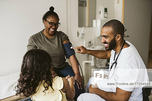 Lachend männlichen Gesundheitswesen Arbeiter Blick auf Mädchen während der Messung Frau Blutdruck in der medizinischen Klinik