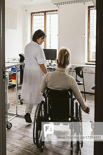 Lächelnder weiblicher medizinischer Experte  der eine behinderte Frau betrachtet  die in einer medizinischen Klinik zu Besuch ist