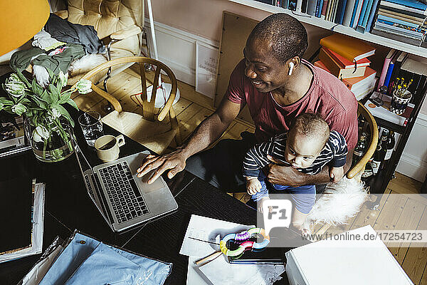 Lächelnde Geschäftsmann mit Laptop  während mit männlichen Kleinkind im Büro zu Hause sitzen