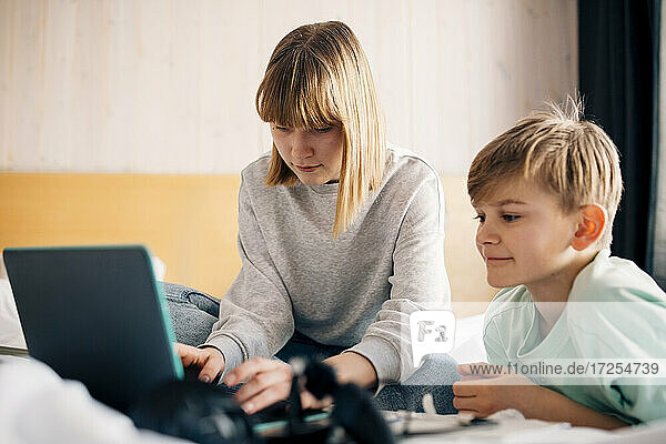 Teenager-Mädchen mit Laptop beim Sitzen von Bruder auf dem Bett zu Hause