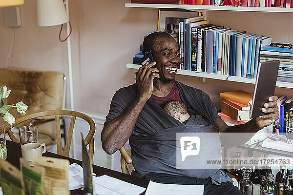 Lächelnde Geschäftsmann spricht auf Smartphone  während hält digitale Tablette im Büro zu Hause