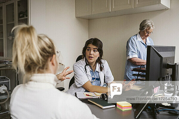 Weiblicher medizinischer Experte im Gespräch mit einer behinderten Frau  während eine ältere Krankenschwester am Schreibtisch arbeitet