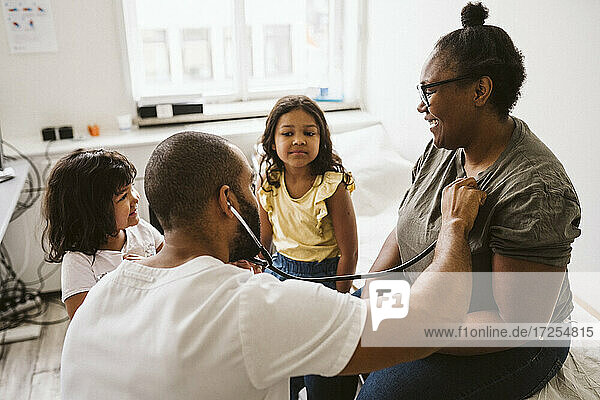 Male healthcare worker with stethoscope examining smiling woman looking at daughter
