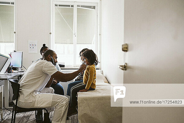 Männlicher Kinderarzt hört den Herzschlag eines Mädchens ab  während er mit einem Stethoskop in einer medizinischen Klinik untersucht