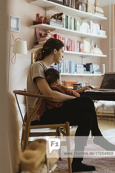 Weibliche professionelle Arbeit am Laptop  während mit Baby Junge im Büro zu Hause sitzen