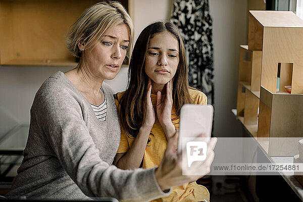 Mutter sitzend mit Tochter erklärt Nackenschmerzen zum Arzt durch Handy zu Hause