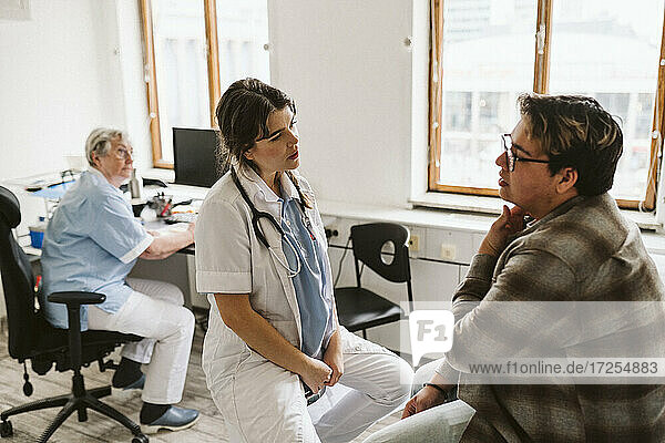 Weiblicher medizinischer Experte bespricht sich mit einem männlichen Patienten  während die Oberschwester am Schreibtisch sitzt