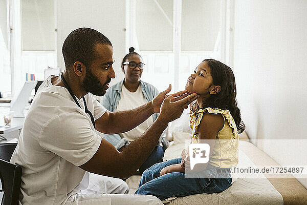 Männlicher Arzt  der den Hals eines Mädchens untersucht  während er in einer medizinischen Klinik sitzt