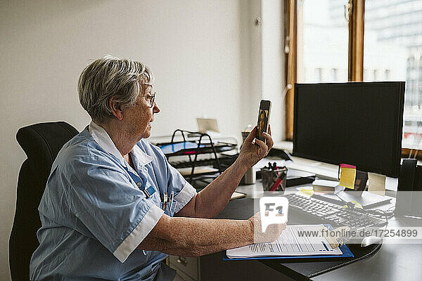 Älterer medizinischer Experte berät Patienten per Videoanruf  während er am Schreibtisch ein Rezept schreibt
