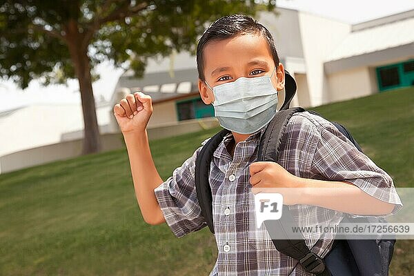 Hispanischer Schüler Junge mit Gesichtsmaske und Rucksack auf dem Schulgelände