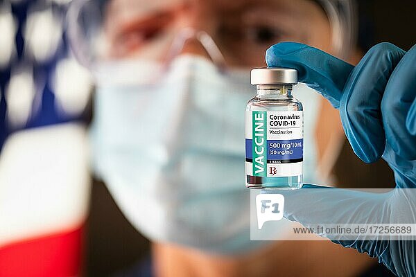 Weibliche medizinische Fachkraft hält Coronavirus Impfstoff Fläschchen in der Nähe von amerikanischen Flagge trägt Schutzmaske und Schutzbrille